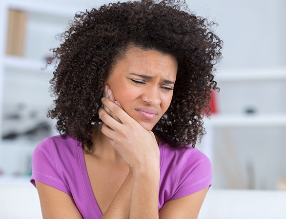 A young woman wearing a purple shirt holding her jaw and cringing in pain