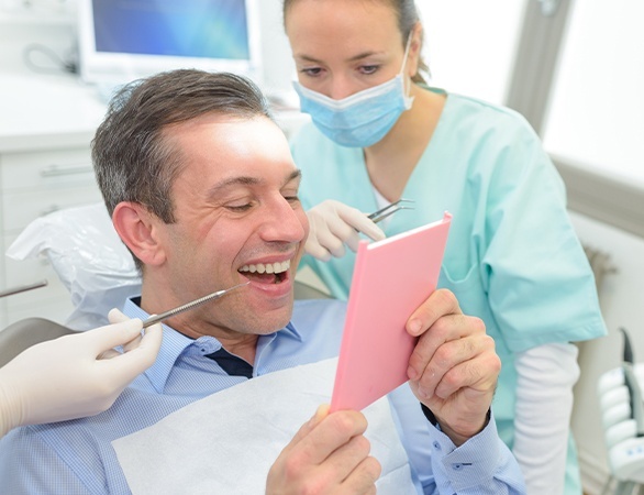 Man in dental chair looking at smile in mirror after full mouth restoration in Aurora