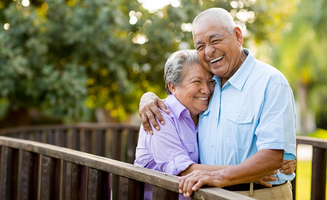 Older couple smiling and hugging outdoors after visiting dentist in Aurora