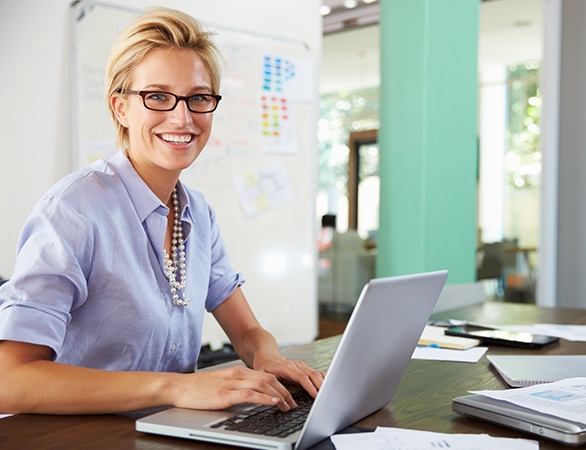 Smiling woman in front of laptop exploring dental treatment financing options with CareCredit