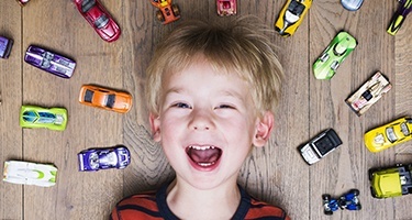 Smiling boy laying on floor with several toy cars