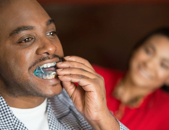 Man sitting on bed and placing oral appliance in his mouth