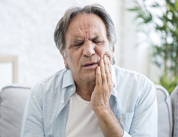 Man in need of TMJ therapy holding his jaw