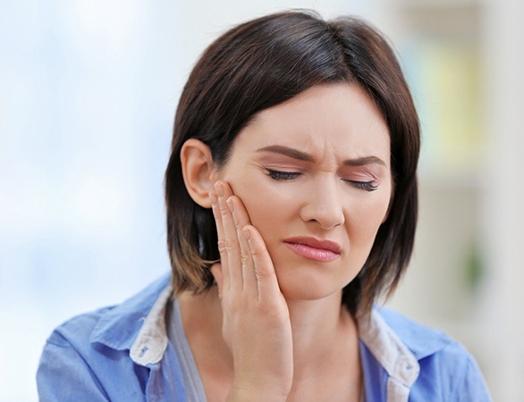 Woman in need of TMJ therapy holding her jaw